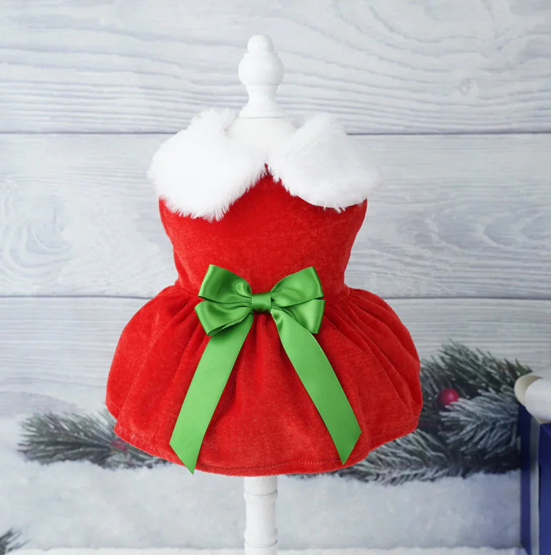Red pet dress with white fur collar and green bow on a mannequin against a wooden background.